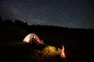 Camping in the mountains and star gazing. Couple sitting outside their camp in the mountains under a starry night sky.